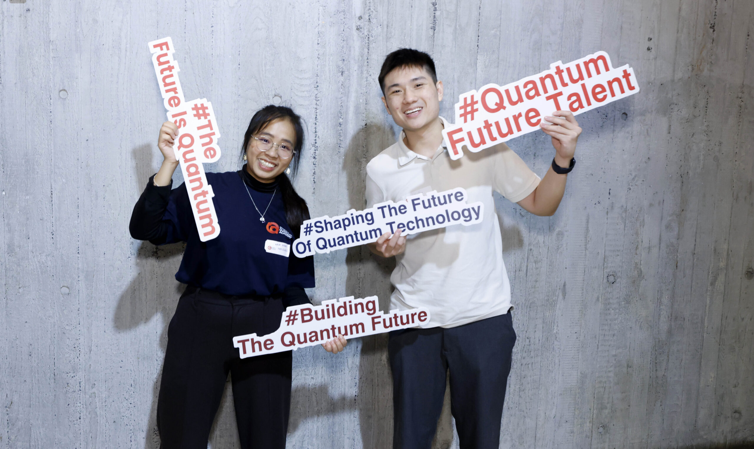 Two attendees at the Quantum Future Talent careers fair stand with props saying #QuantumFutureTalent, #TheFutureIsQuantum, #ShapingTheFutureofQuantumTechnology and #BuildingTheQuantumFuture